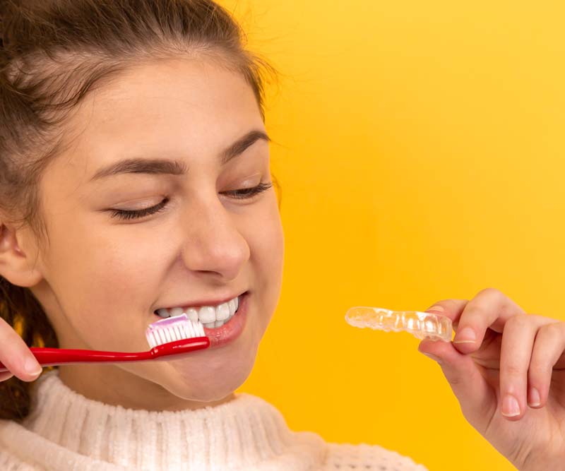 Girl Holding Invisalign Tray while Brushing Teeth